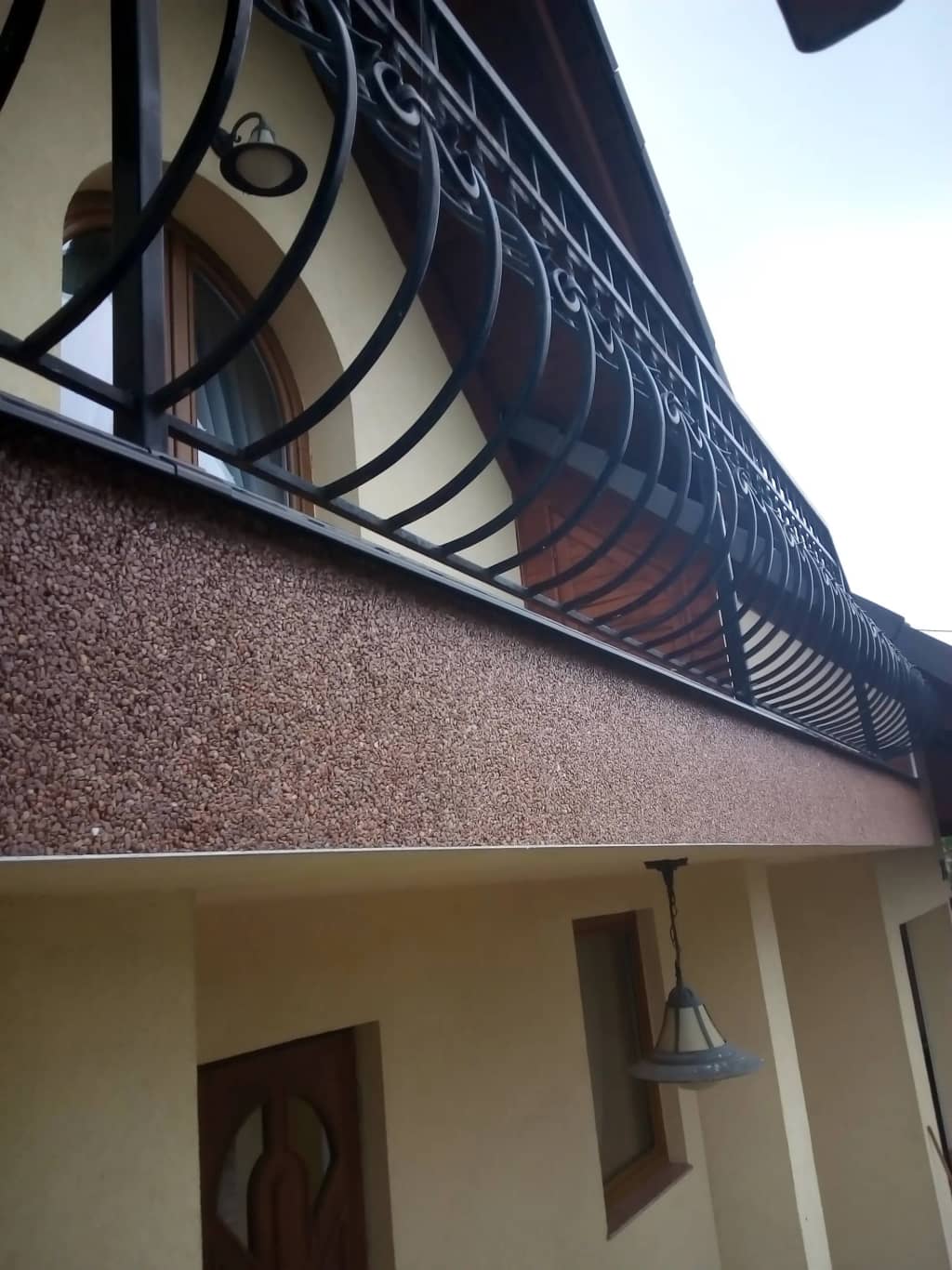 Brązowy kamienny dywan na balkonie z kutą balustradą i cokołem