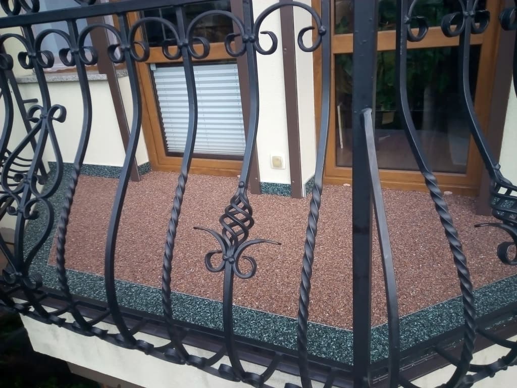 Ceglasty kamienny dywan na balkonie z kutą balustradą