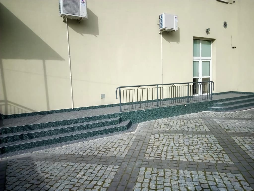 Kamienny dywan na pochylni i stopniach przy elewacji budynku