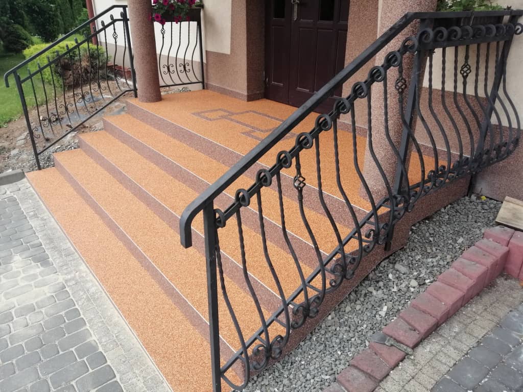 Pomarańczowy kamienny dywan na schodach z kutą balustradą
