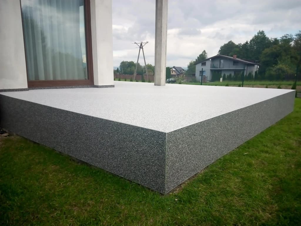 Kamienny dywan na tarasie z ciemną krawędzią wyprowadzoną na bok płyty