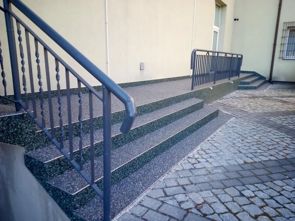 Kamienny dywan na schodach wejściowych z metalową balustradą