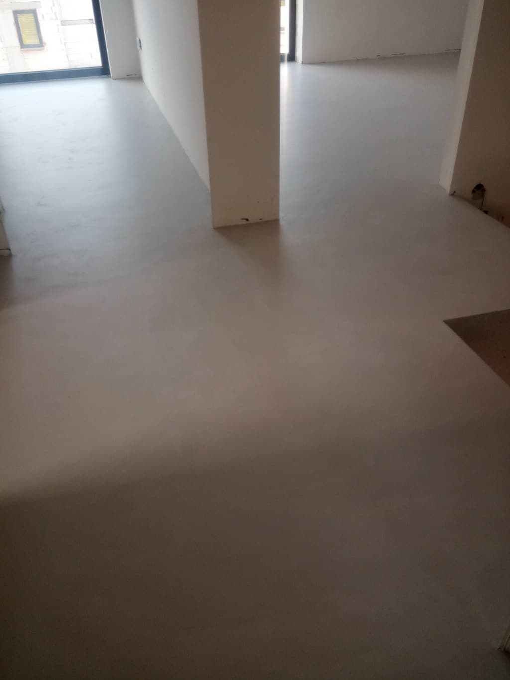 Beżowa podłoga z mikrocementu w otwartej przestrzeni dziennej z przeszkleniem