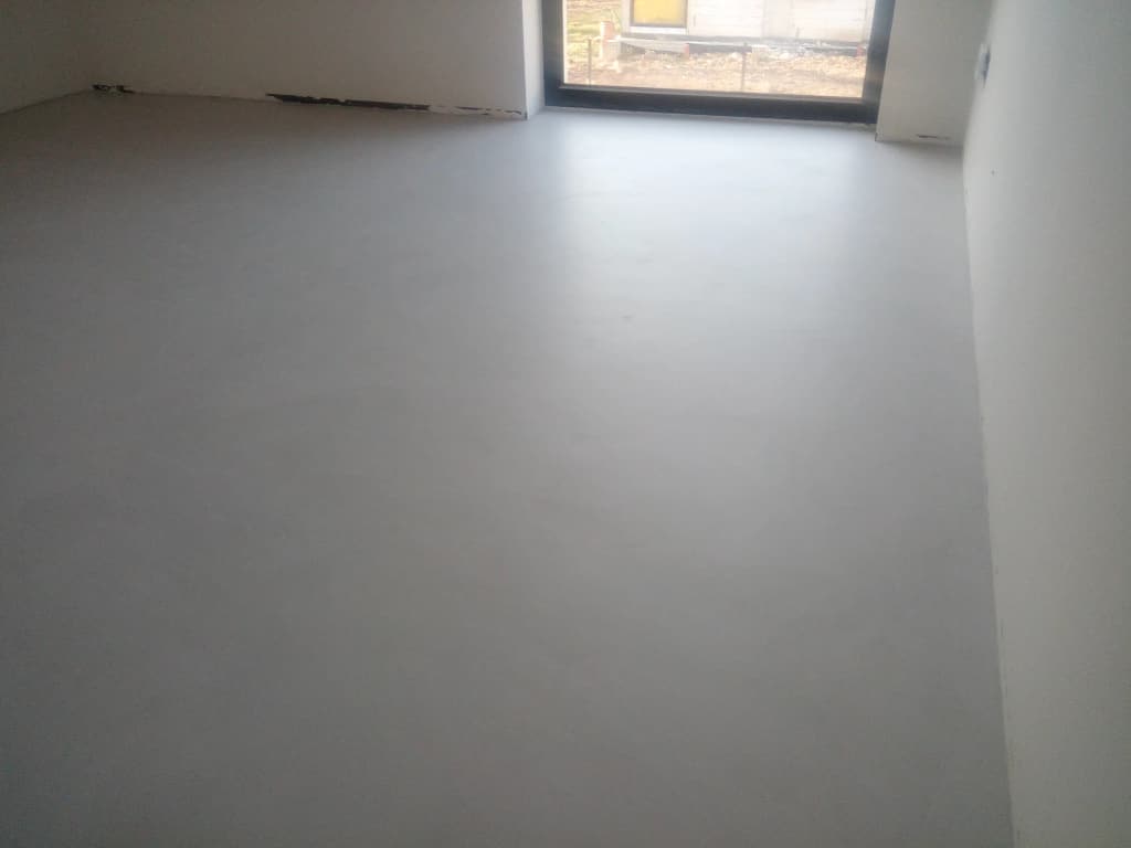 Gładka szara podłoga z mikrocementu w pokoju z oknem