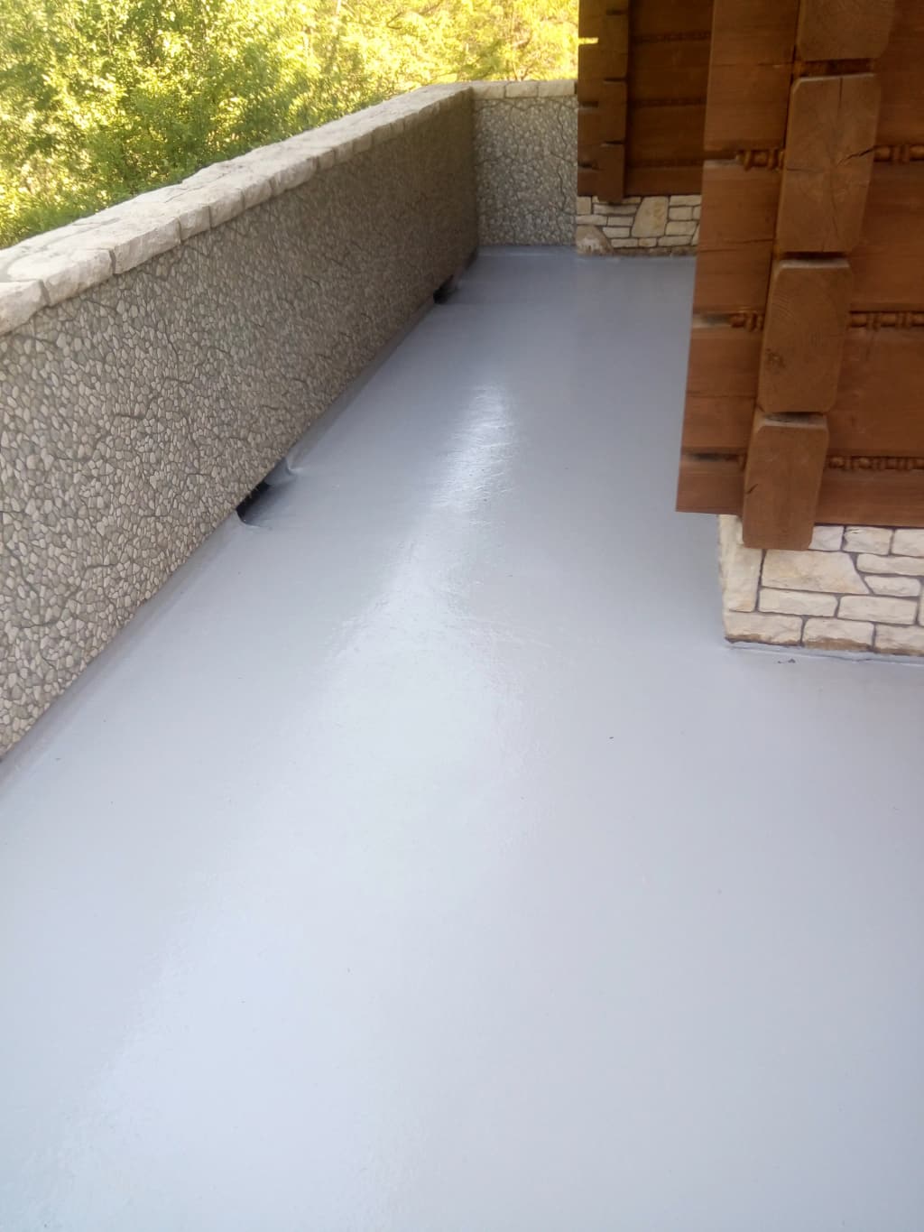 Szara powłoka żywiczna na balkonie wyprowadzona na cokół przy kamiennej balustradzie