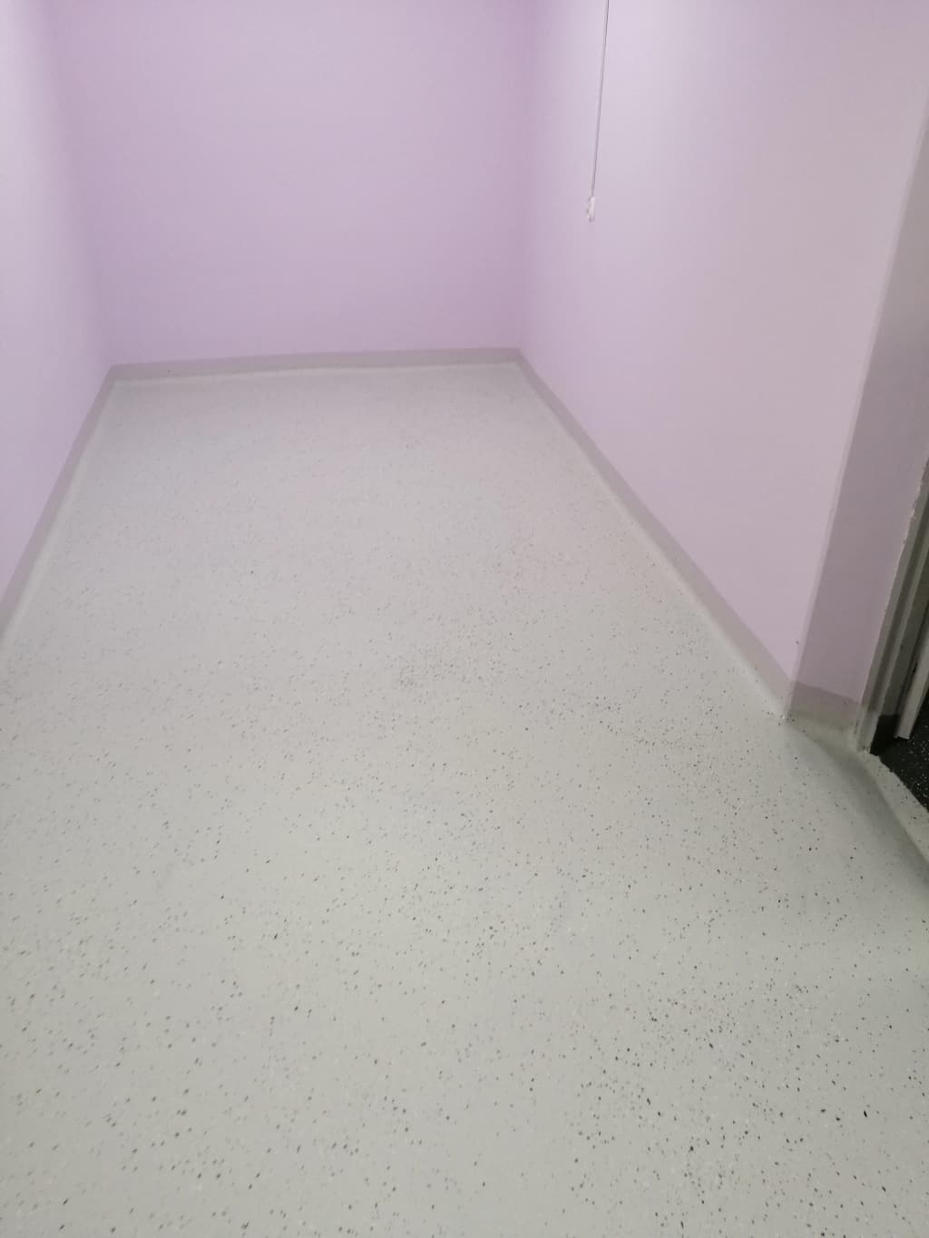 Biała posadzka żywiczna z drobnymi ciemnymi płatkami w niewielkim pomieszczeniu z cokołem